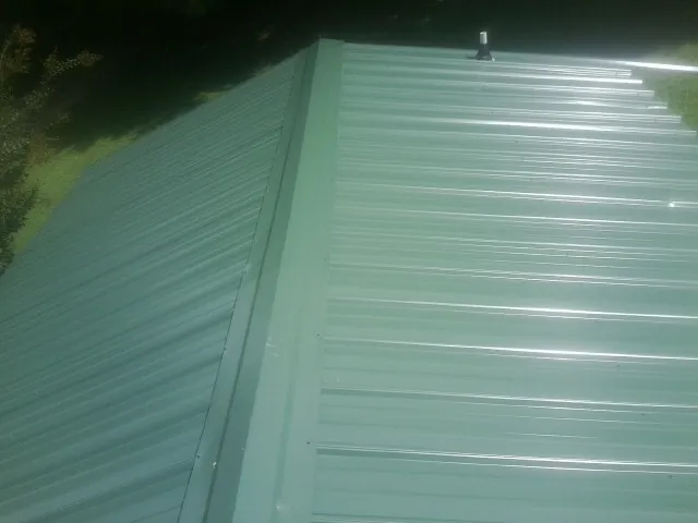 New green metal panels meeting at the ridge of a roof — Flat Roof Repair work by our crew in Greenwood
