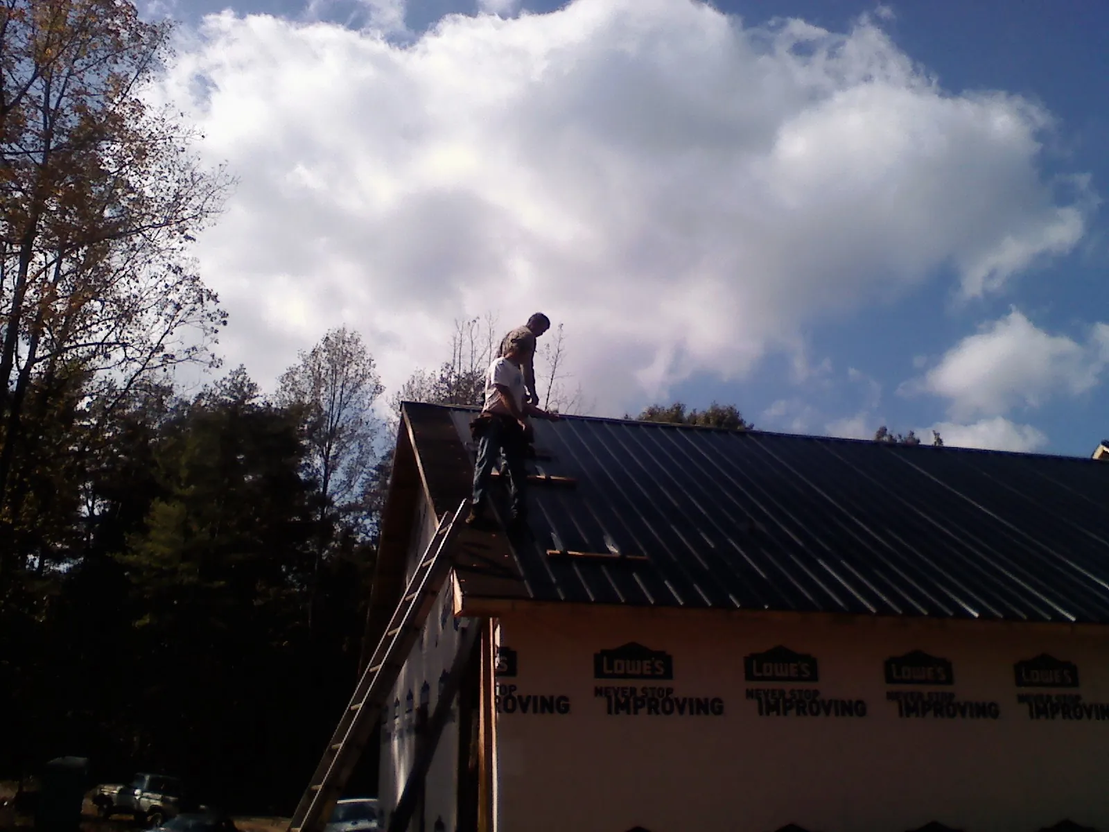 Roofer fastening dark metal panels high against a cloudy sky, from a Roof Inspection job in Greenwood